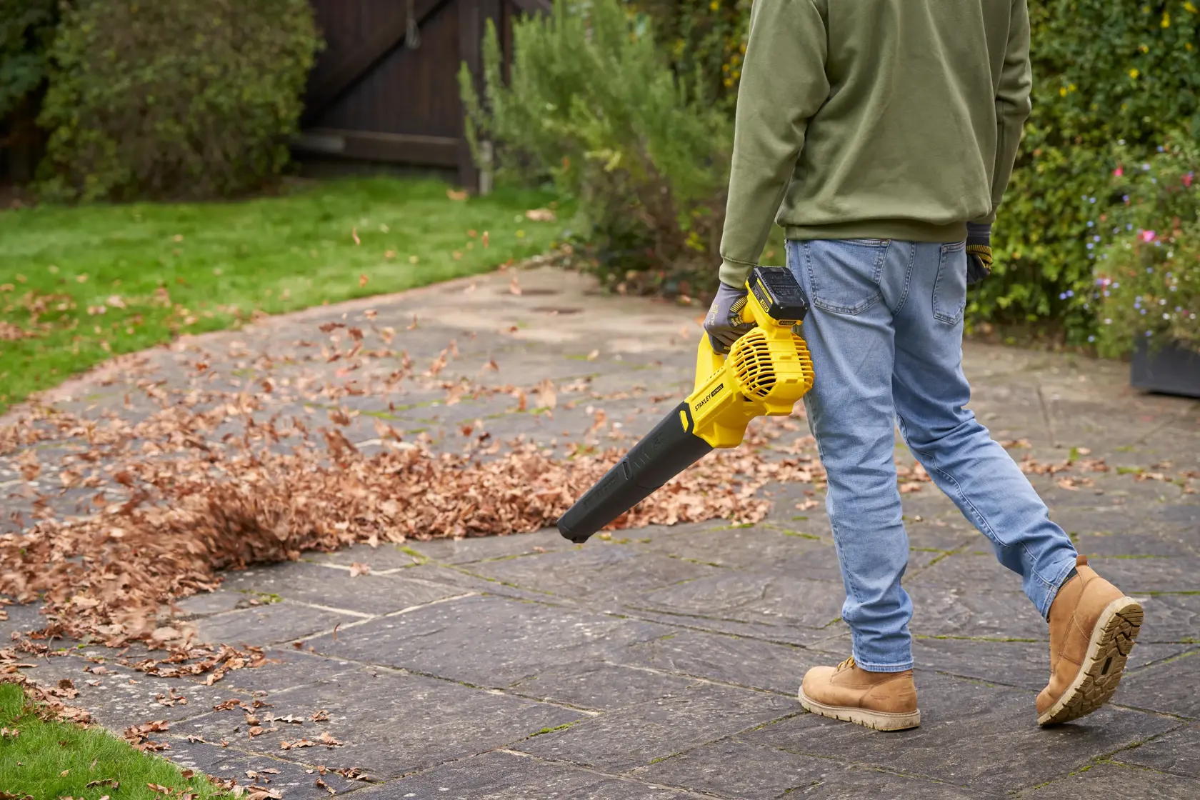 STANLEY SFMCBL714M1 leaf blower in use clearing leaves on patio, outdoor setting, side angle.