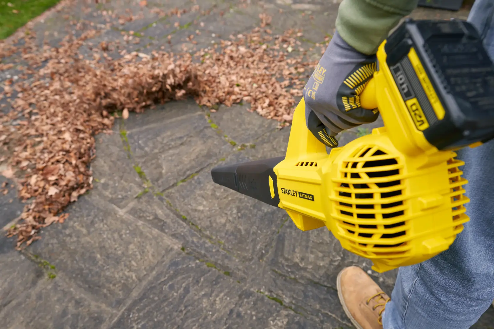 STANLEY SFMCBL714M1 leaf blower in use on outdoor stone patio, moving a pile of dry leaves.