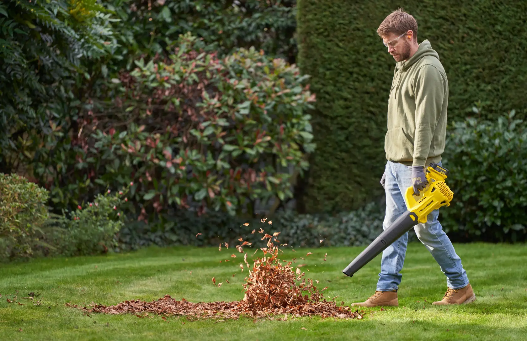 STANLEY SFMCBL714M1 leaf blower in use outdoors, blowing leaves on a green lawn.