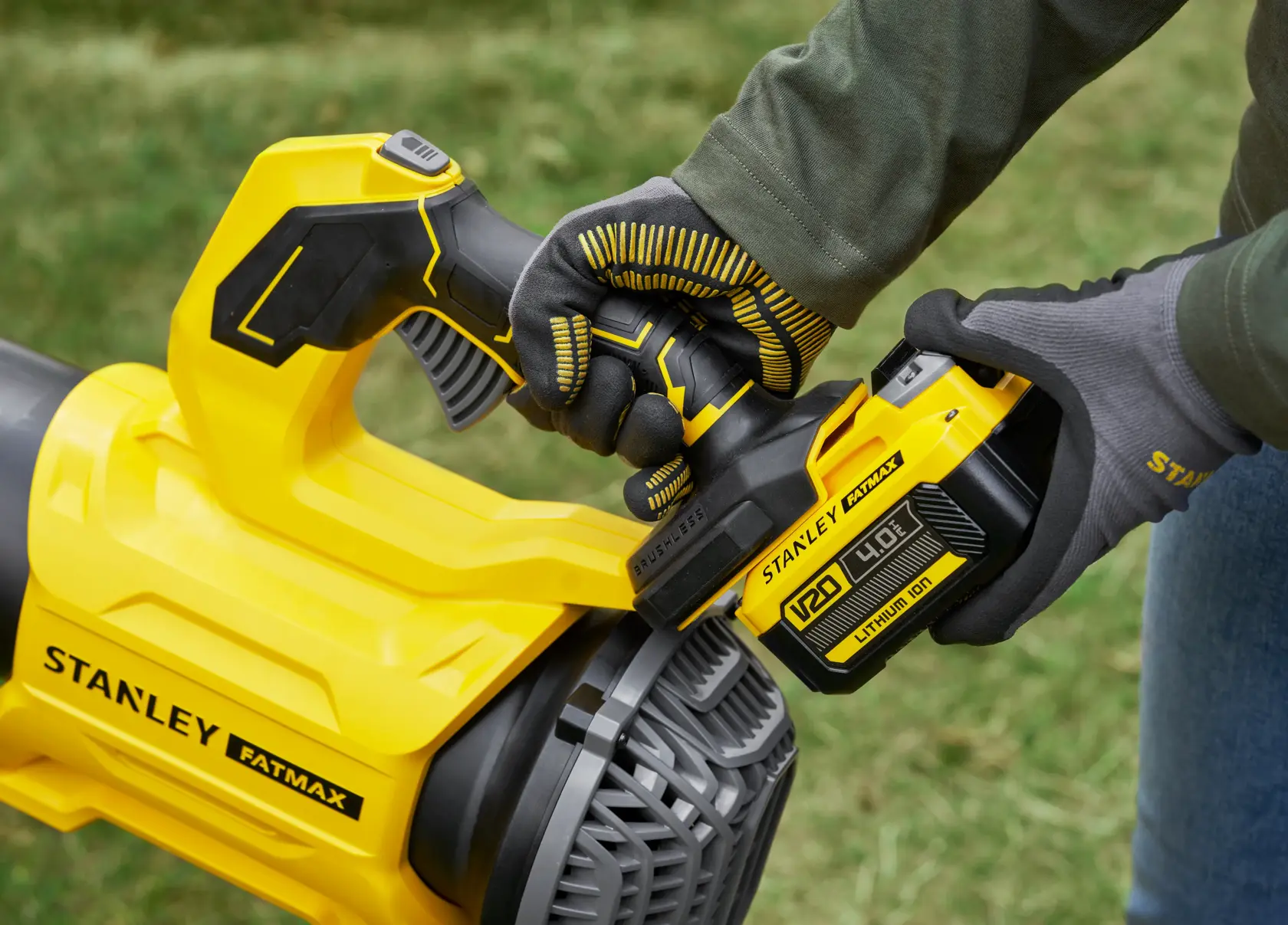 STANLEY SFMCBL730B leaf blower close-up, yellow handle and battery, outdoor use, person with gloves.