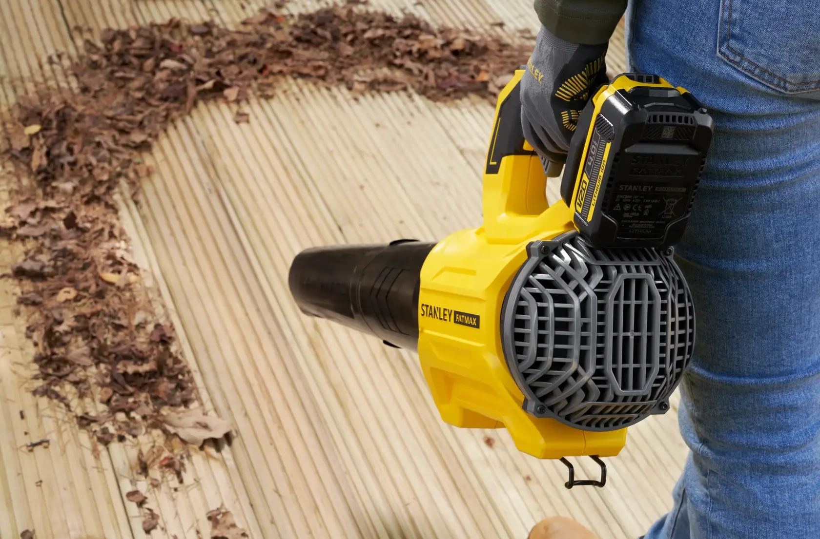 STANLEY SFMCBL730B leaf blower in use on wooden deck, clearing dry leaves, side view.