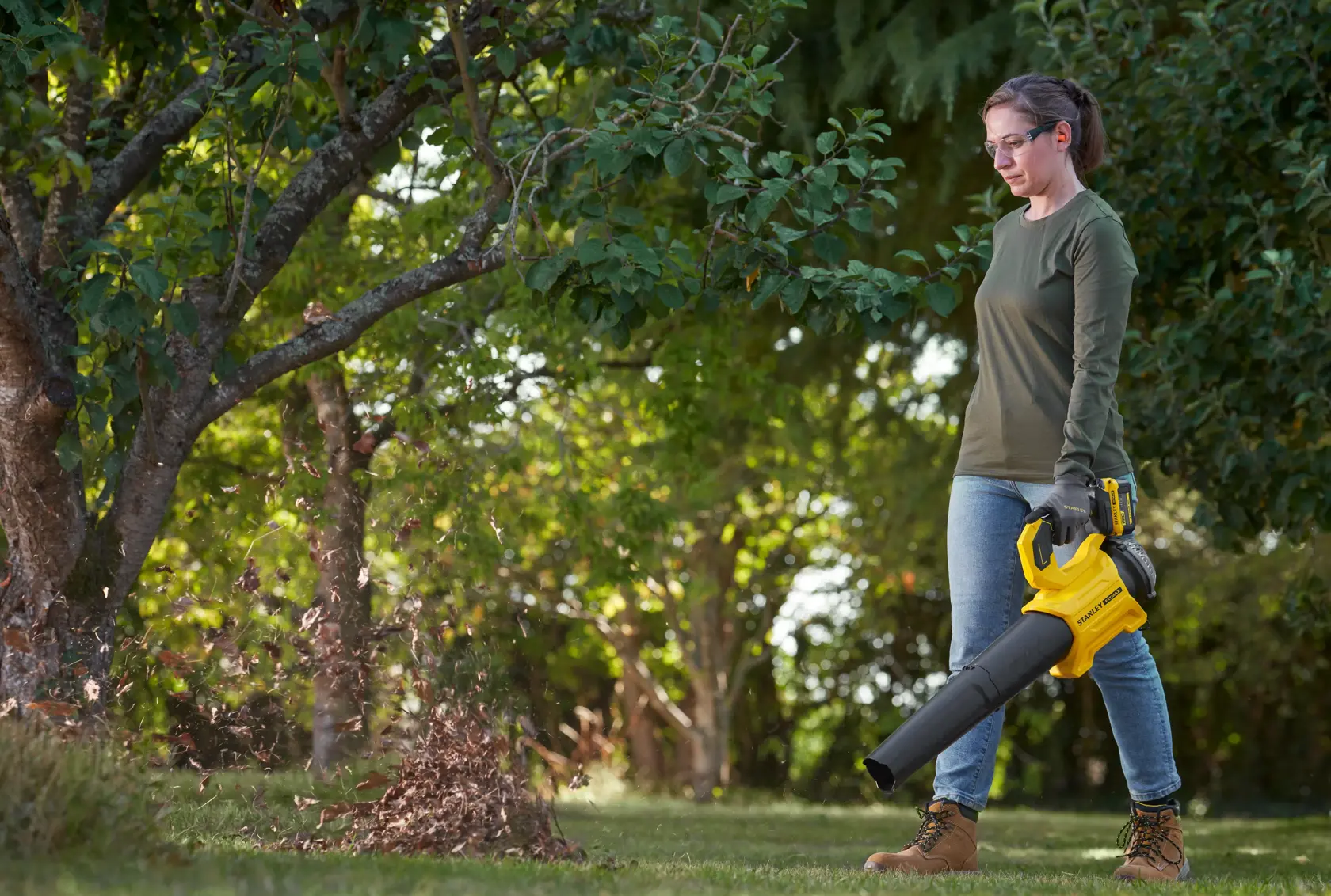 STANLEY SFMCBL730M1 leaf blower in use outdoors, yellow and black handheld cordless tool blowing leaves.
