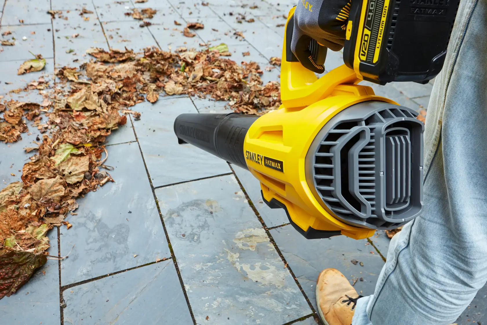 STANLEY SFMCBL7B leaf blower on patio, yellow and black design, photographed in use clearing dry leaves.