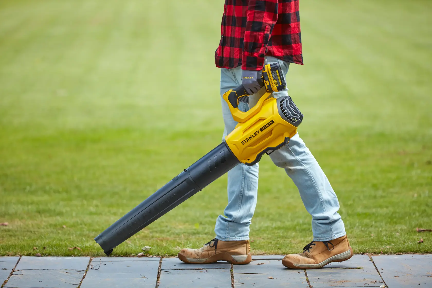 Stanley SFMCBL7B leaf blower held by person outdoors on grass wearing jeans and boots.