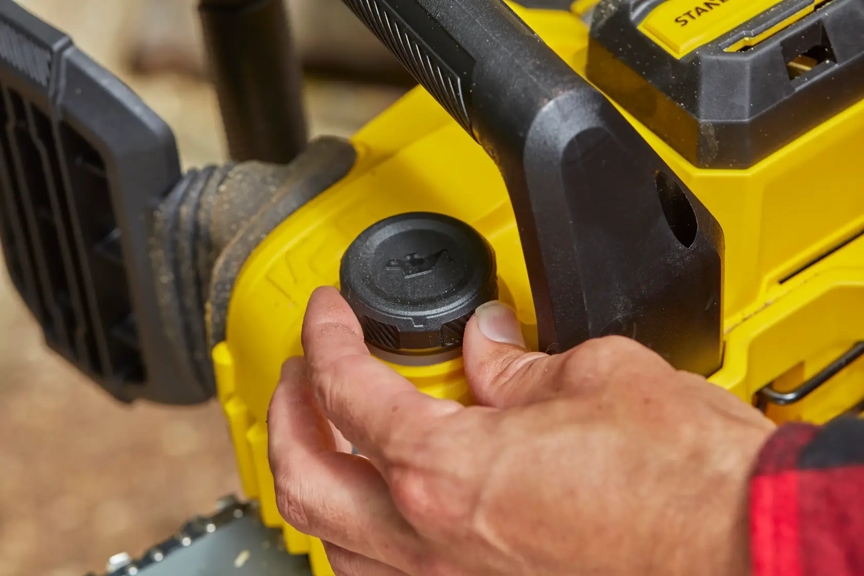 STANLEY SFMCCS630M1 chainsaw close-up, hand adjusting oil cap, yellow and black design, outdoor setting.