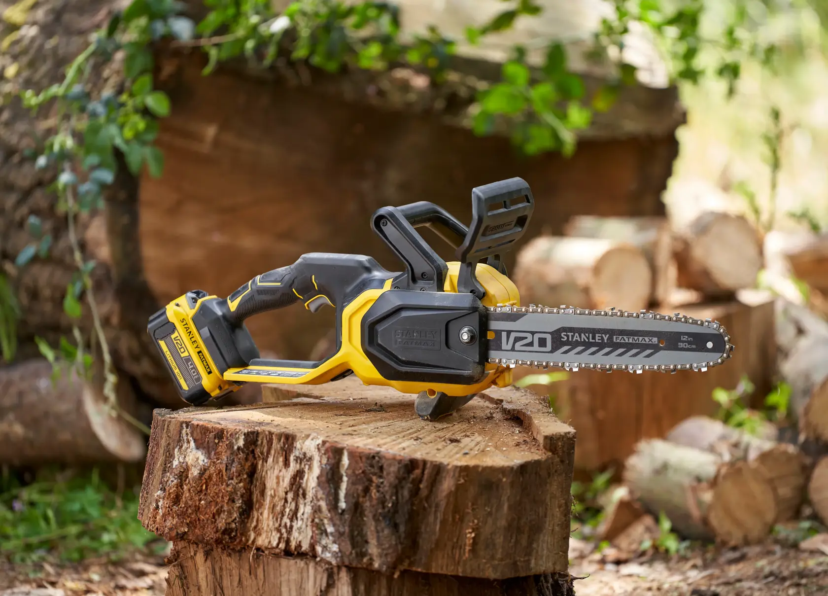 STANLEY SFMCCS730B cordless chainsaw with yellow and black body, resting on a cut tree stump outdoors.