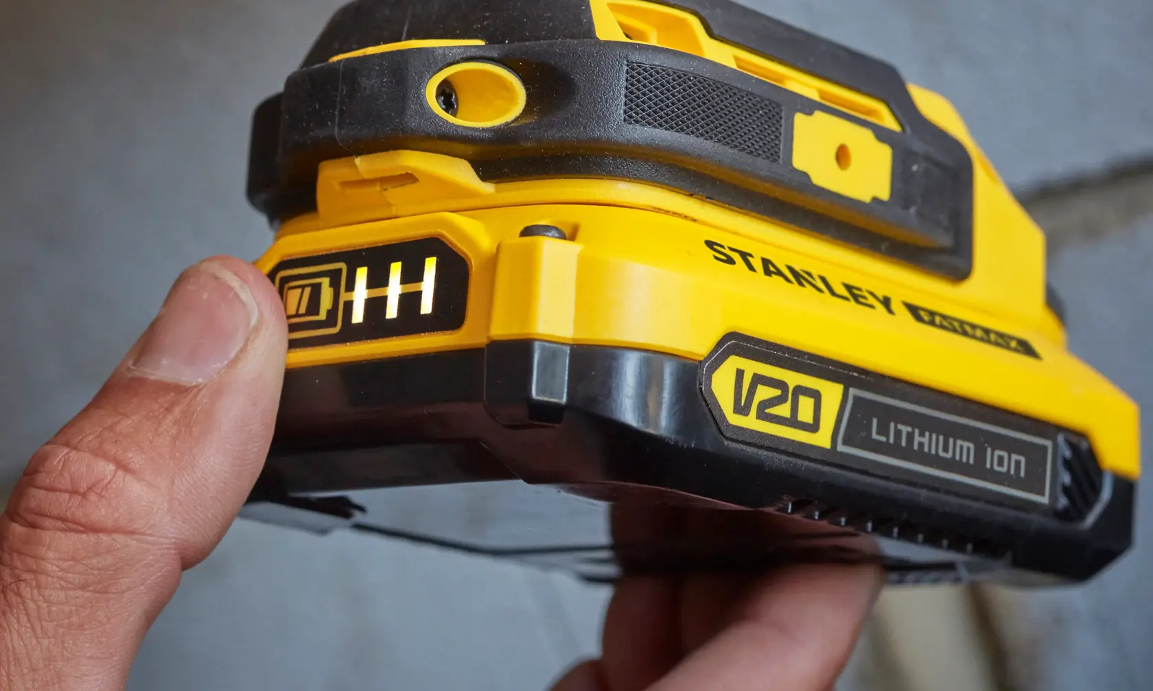 Stanley SFMCD711B V20 Lithium Ion battery close-up, yellow and black casing, finger pressing indicator.