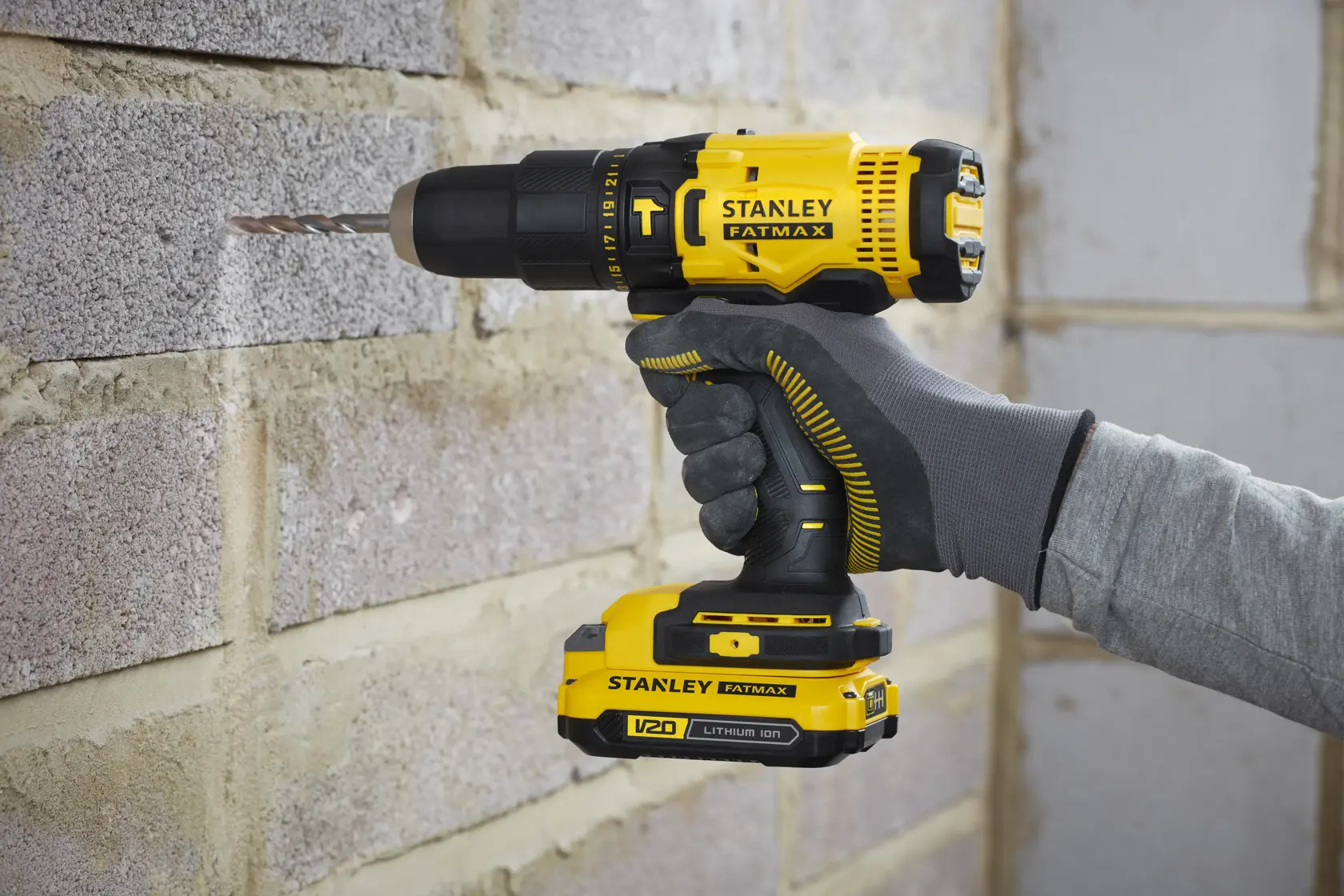 Stanley SFMCD711B yellow cordless drill in use on a brick wall, FATMAX branding visible.