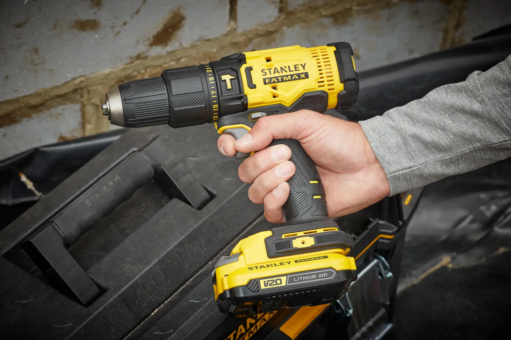 STANLEY SFMCD711DM2 cordless drill in yellow and black, held in hand near toolbox, close-up side view.