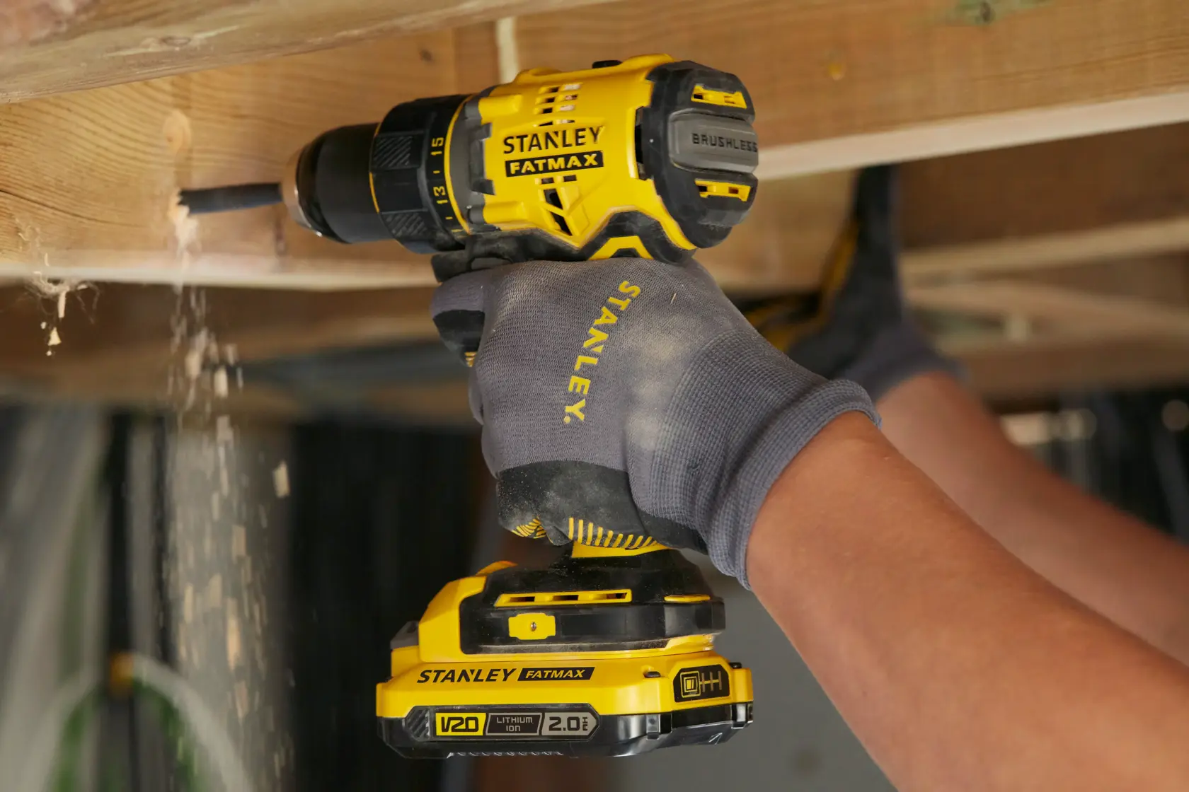 Stanley SFMCD720DR2 brushless cordless drill in use under wooden beam, yellow and black design.