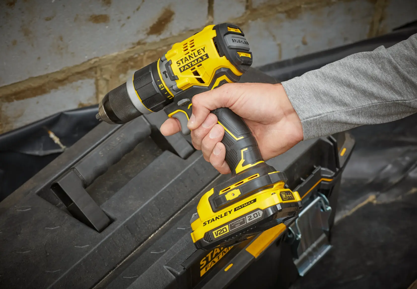 Photo of STANLEY SFMCD721B cordless drill in use, yellow and black, held above toolbox.