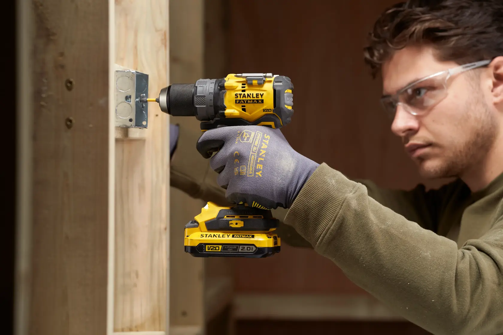 Photo of STANLEY SFMCD725D2K cordless drill in use on wooden frame, close side view, worker wearing gloves.