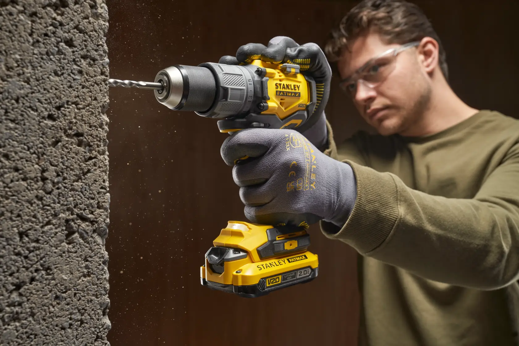 Photo of STANLEY SFMCD726B cordless drill in use, drilling into concrete, close-up on yellow and black tool.