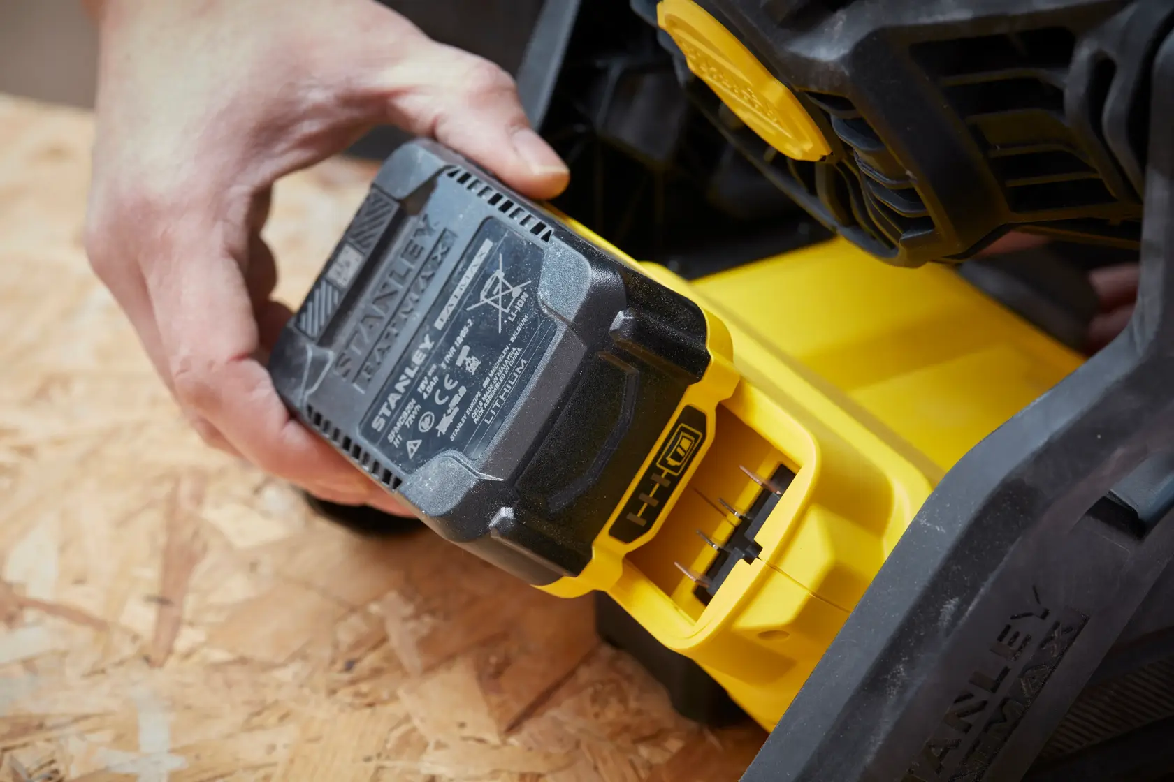 Photo of STANLEY SFMCE001B battery being inserted into a yellow power tool on a wood surface.
