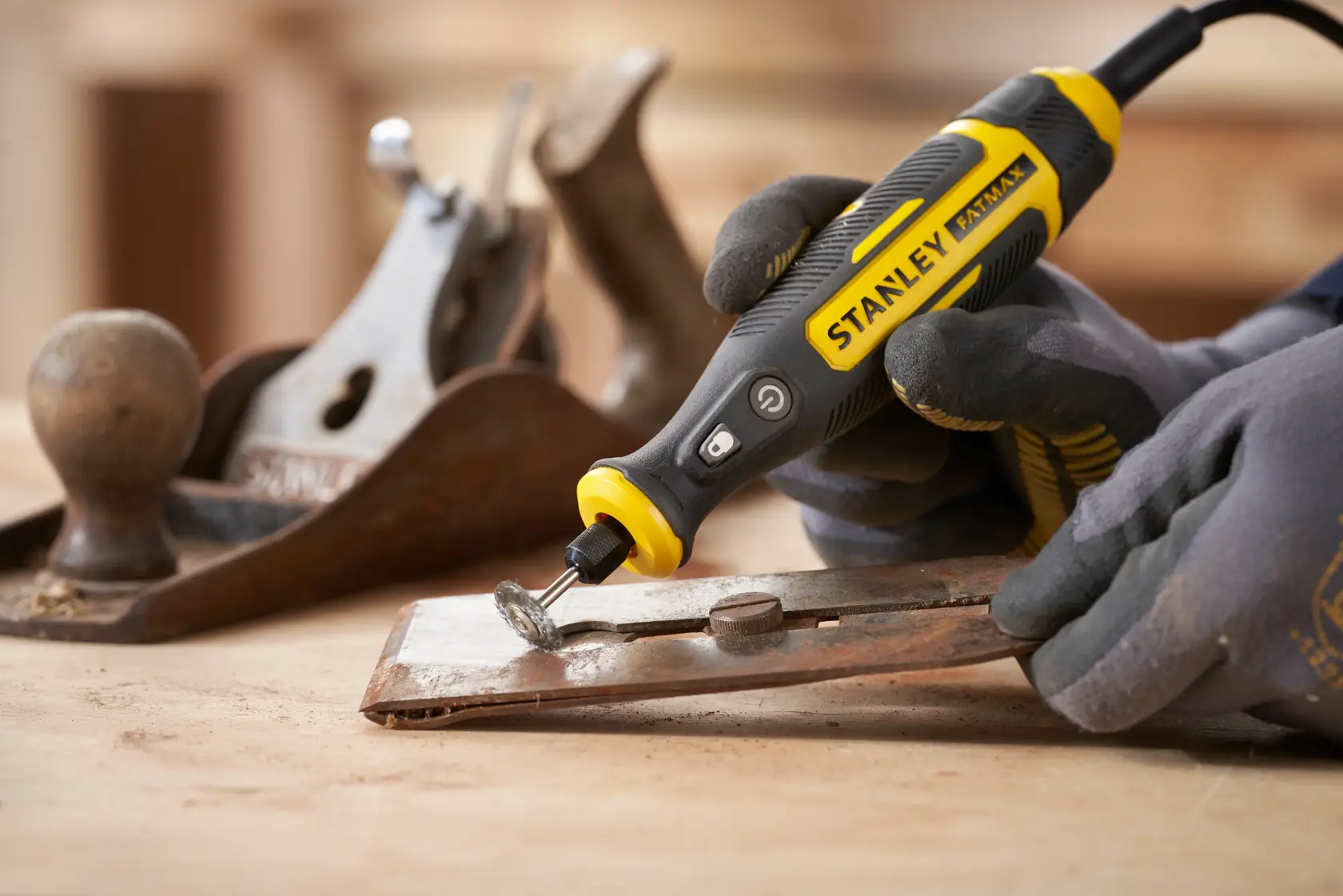 Photo of STANLEY SFMCE030B rotary tool being used to grind metal, handled with gloves, woodworking tools nearby.