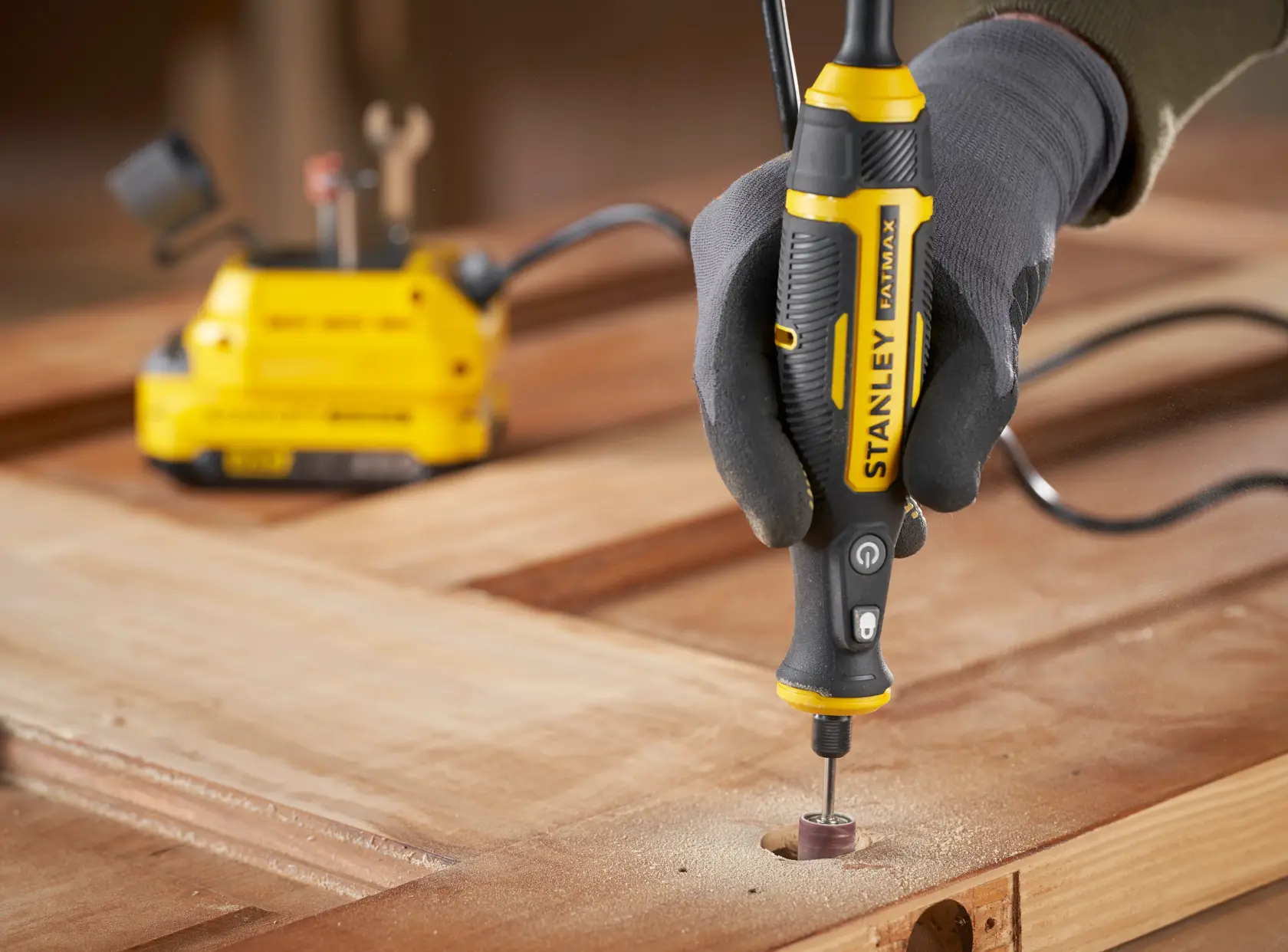 STANLEY SFMCE030B rotary tool used for sanding wood, close-up view of tool in hand on work surface.