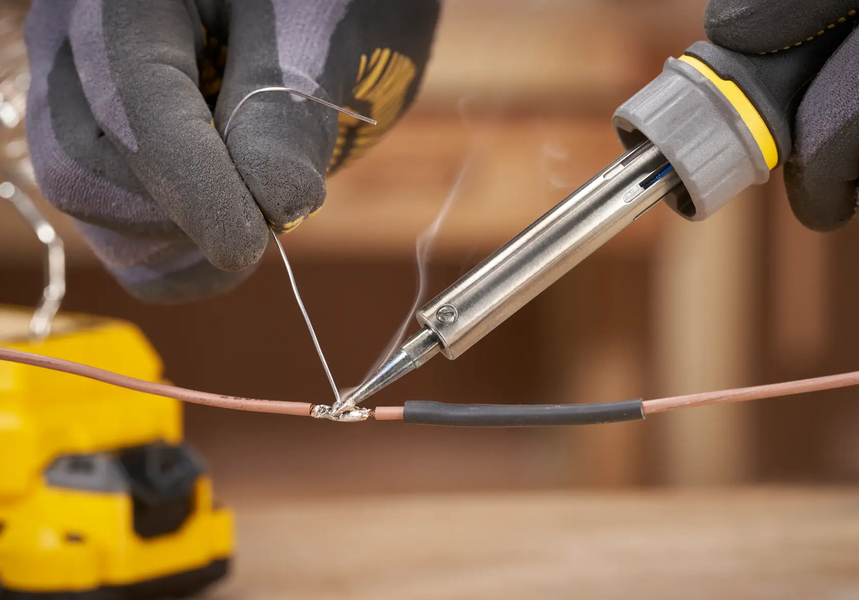 STANLEY SFMCE040B soldering iron in use, close-up, joining wires with solder, gloved hands visible.