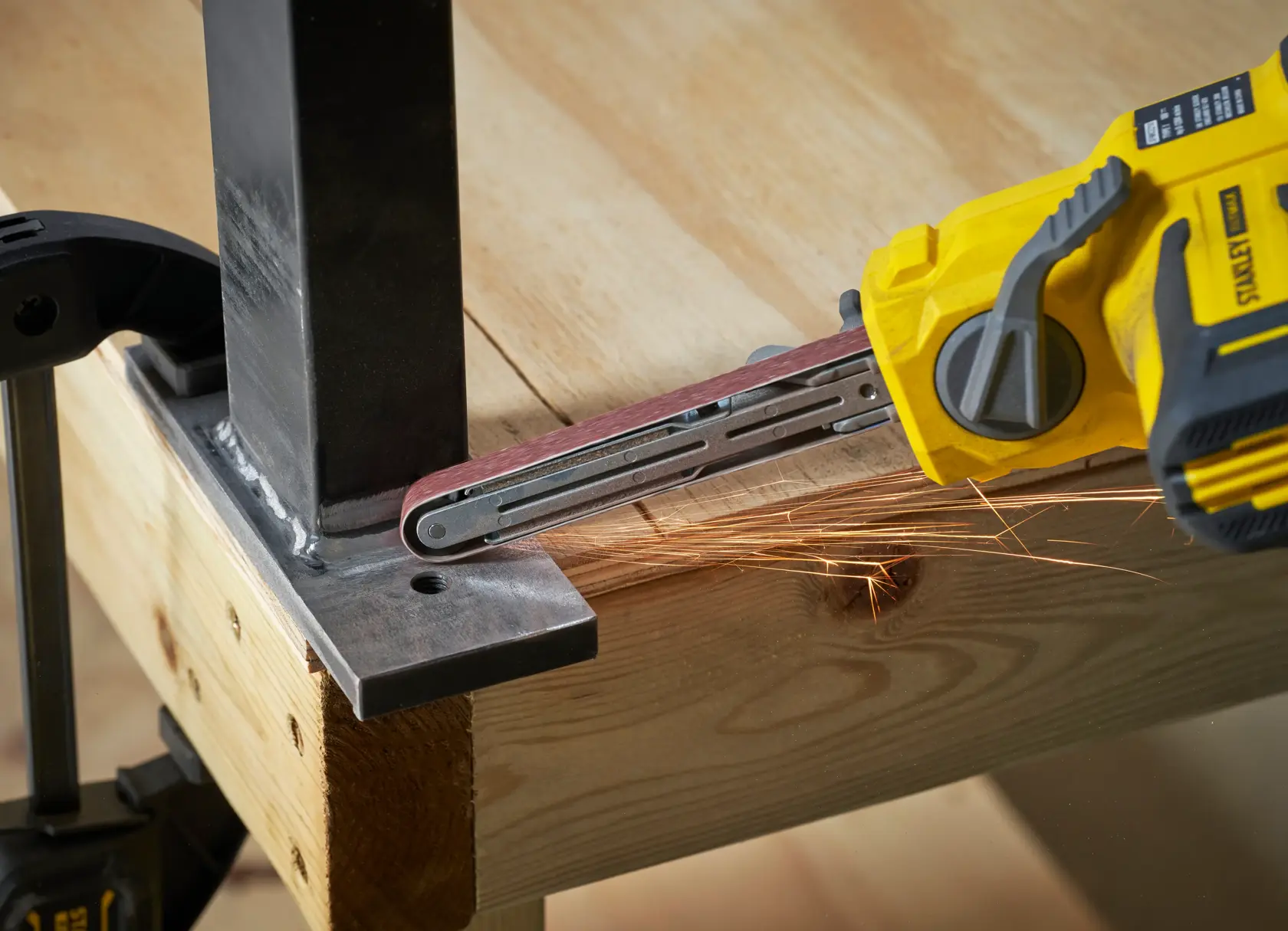 STANLEY SFMCE210B cordless belt file grinder sanding metal joint, close-up angle.
