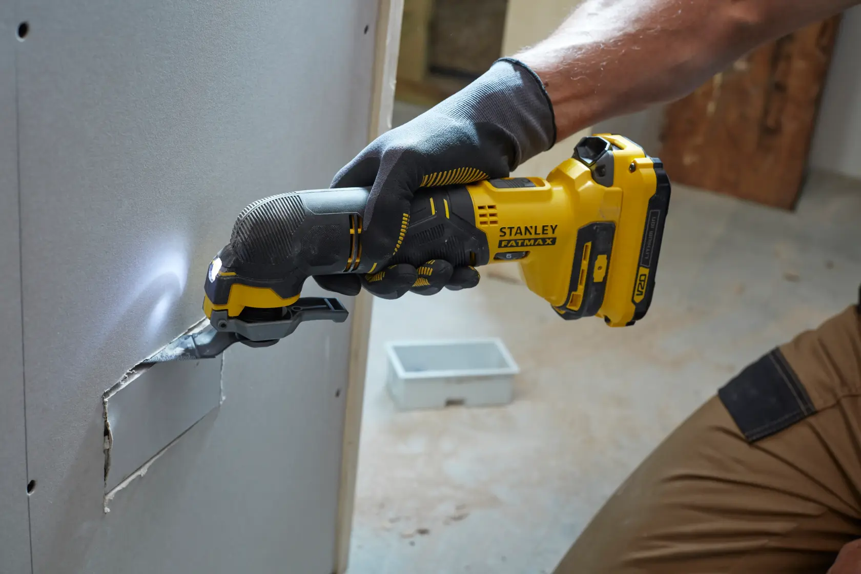 STANLEY SFMCE500B oscillating multi-tool cutting drywall, worker wearing gloves, tool features yellow and black design.