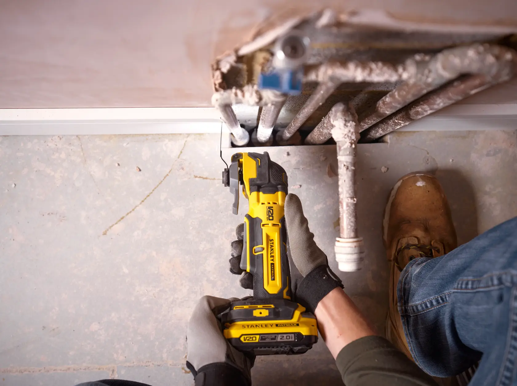 Photo of STANLEY SFMCE510B oscillating multi-tool cutting beside pipes on a concrete floor.