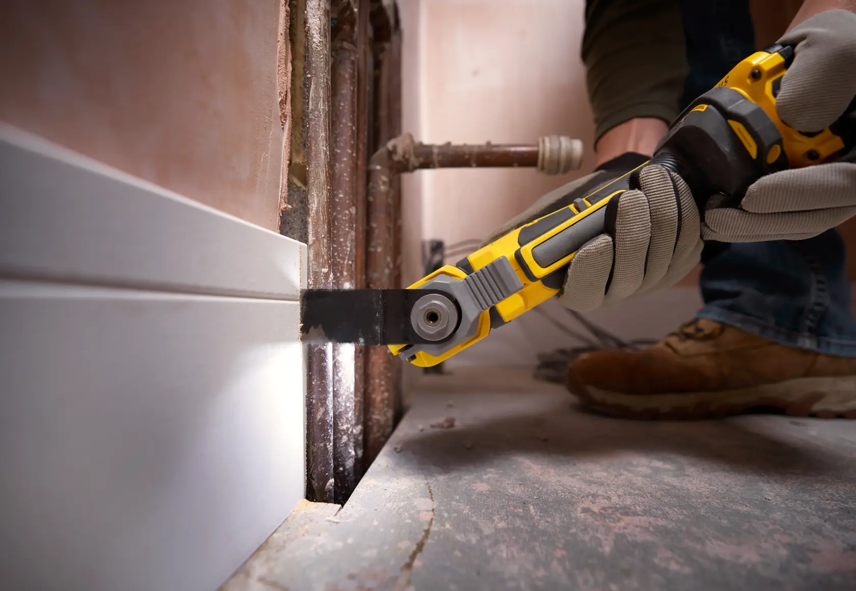 STANLEY SFMCE510B oscillating multi-tool cutting baseboard near pipes, handheld close-up during renovation.