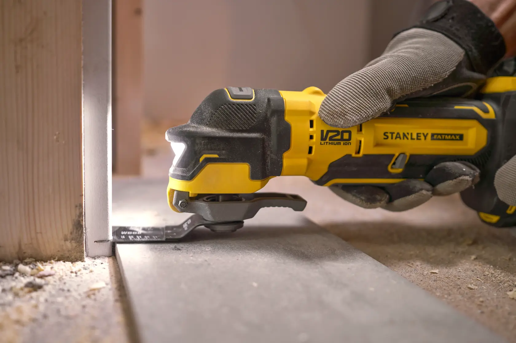 Stanley SFMCE510M2K oscillating multi-tool cutting floor panel, close-up with gloved hand, construction setting.