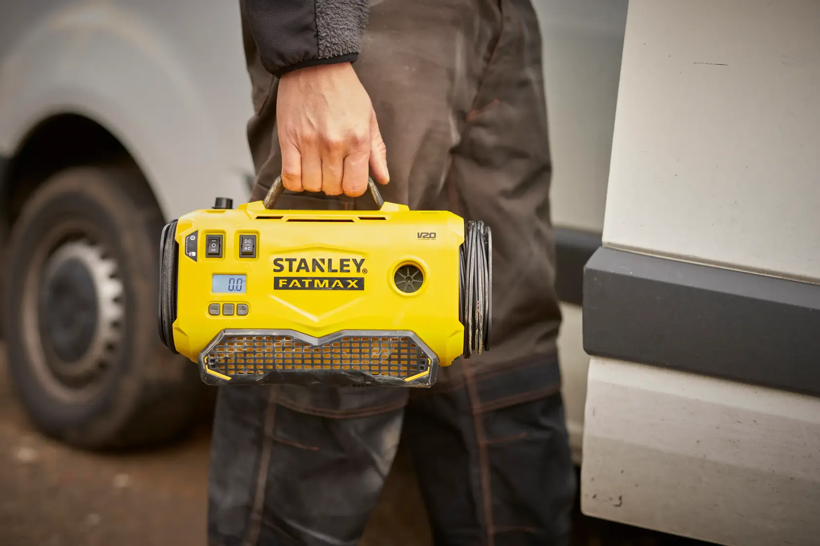 Stanley SFMCE520B portable yellow inflator held by handle, taken outdoors near vehicle.