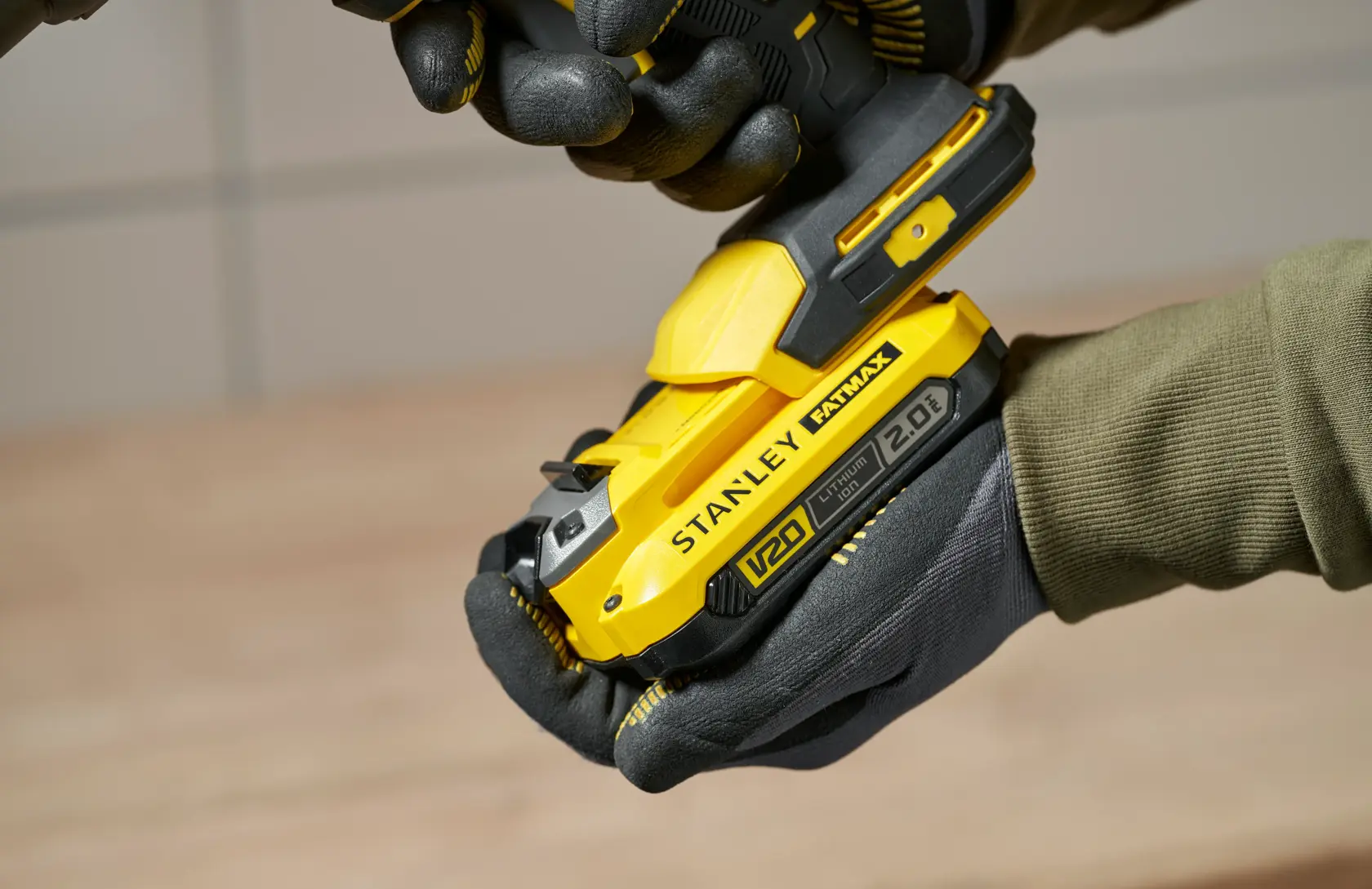 Photo of STANLEY SFMCE600B yellow cordless tool in gloved hands, close-up side view.