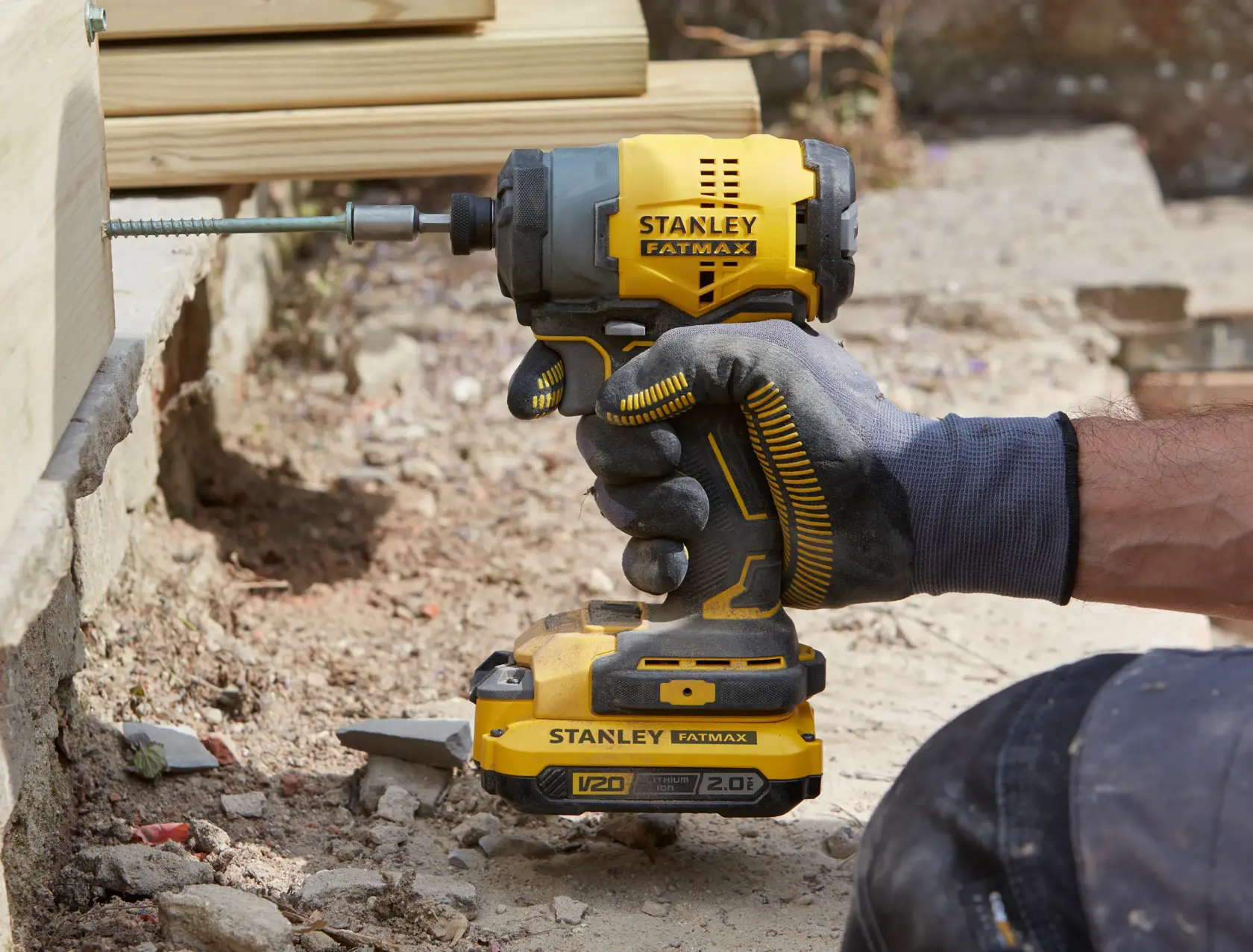 Stanley SFMCF810B impact driver held by gloved hand driving screw into wood, outdoor construction setting.