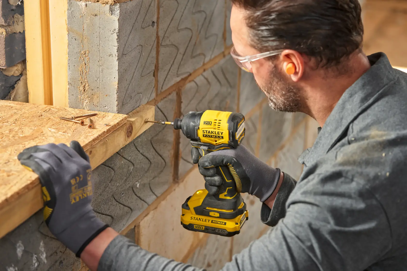Photo of worker using STANLEY SFMCF811B-XJ cordless impact driver on wood near brick wall, wearing gloves.