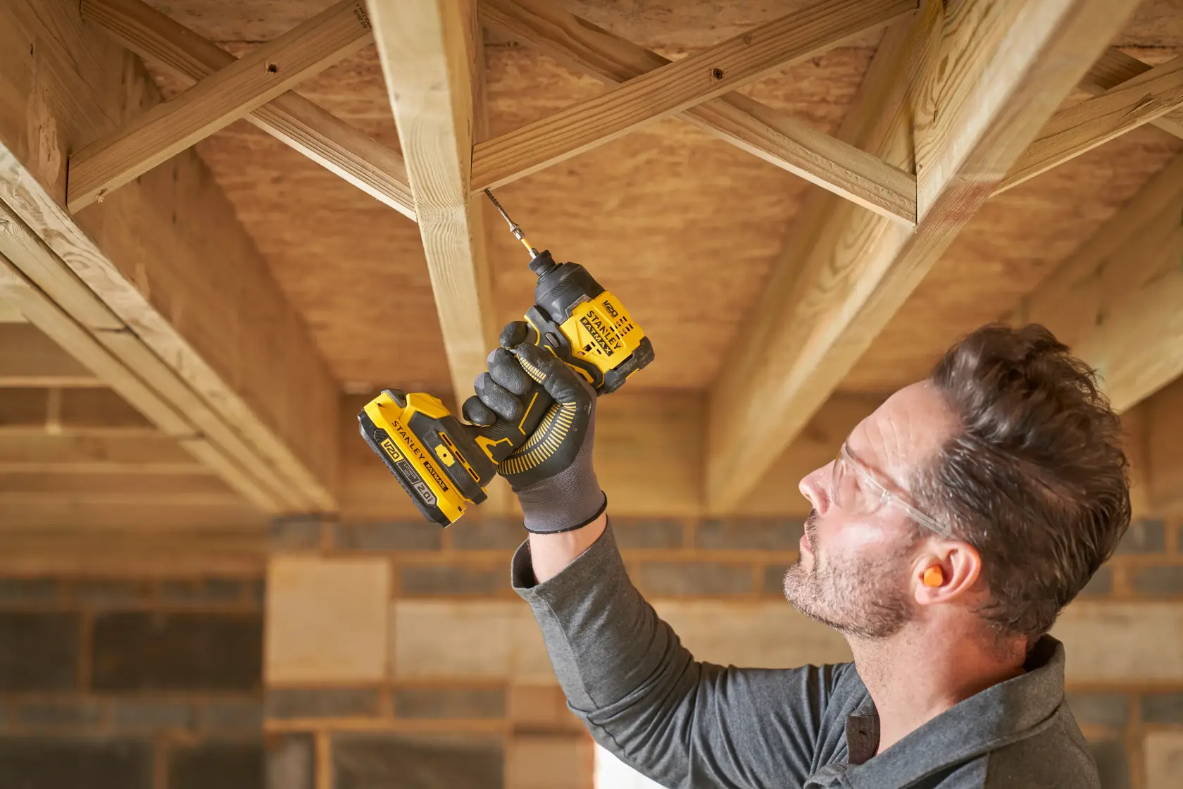 Photo of person using STANLEY SFMCF811B-XJ cordless drill to fasten screw into wooden ceiling frame.
