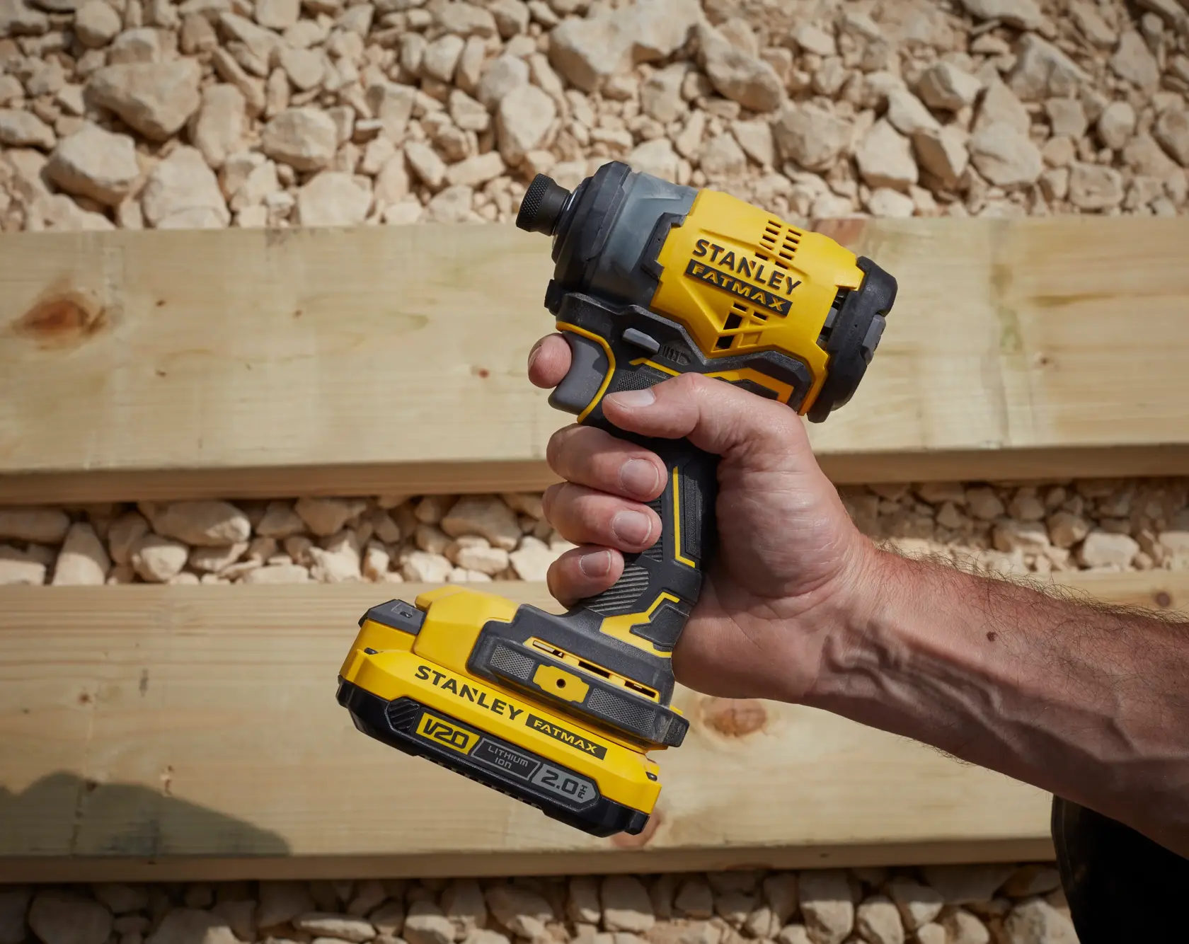 Stanley SFMCF820B impact driver held in hand, yellow and black, outdoor work site, side angle.