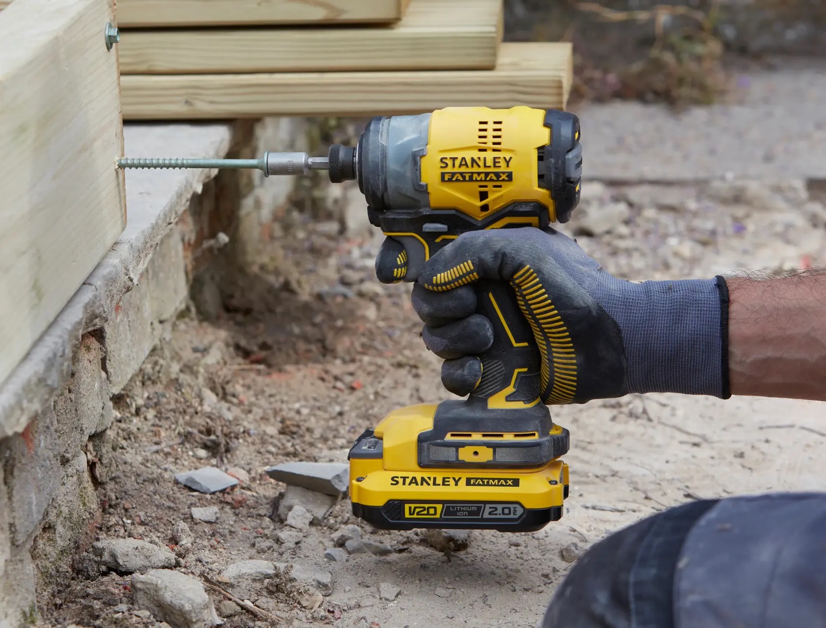 STANLEY SFMCF820B cordless impact driver in use, yellow and black, driving a screw into wood outdoors.