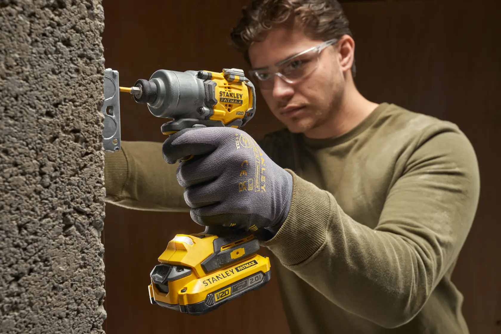 STANLEY SFMCF830B cordless impact driver in use, yellow and black, drilling into concrete wall.