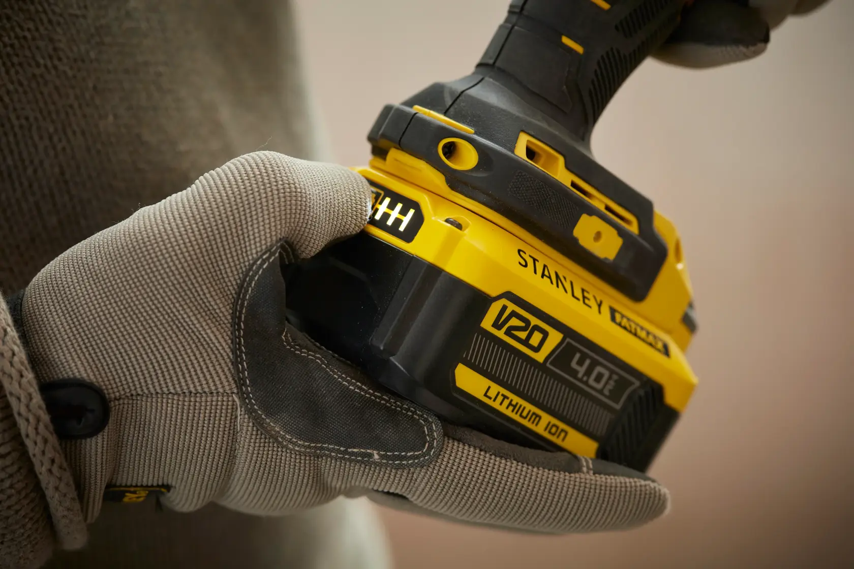 Photo of STANLEY SFMCF900B cordless tool held by gloved hand, showing V20 4.0Ah lithium-ion battery detail.