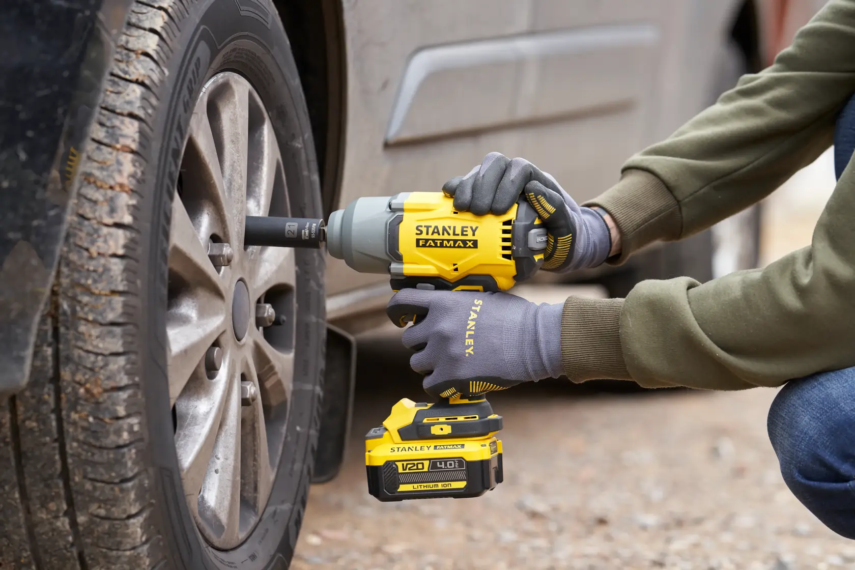 Photo of STANLEY SFMCF940B cordless impact wrench being used to tighten a car wheel lug nut outdoors.