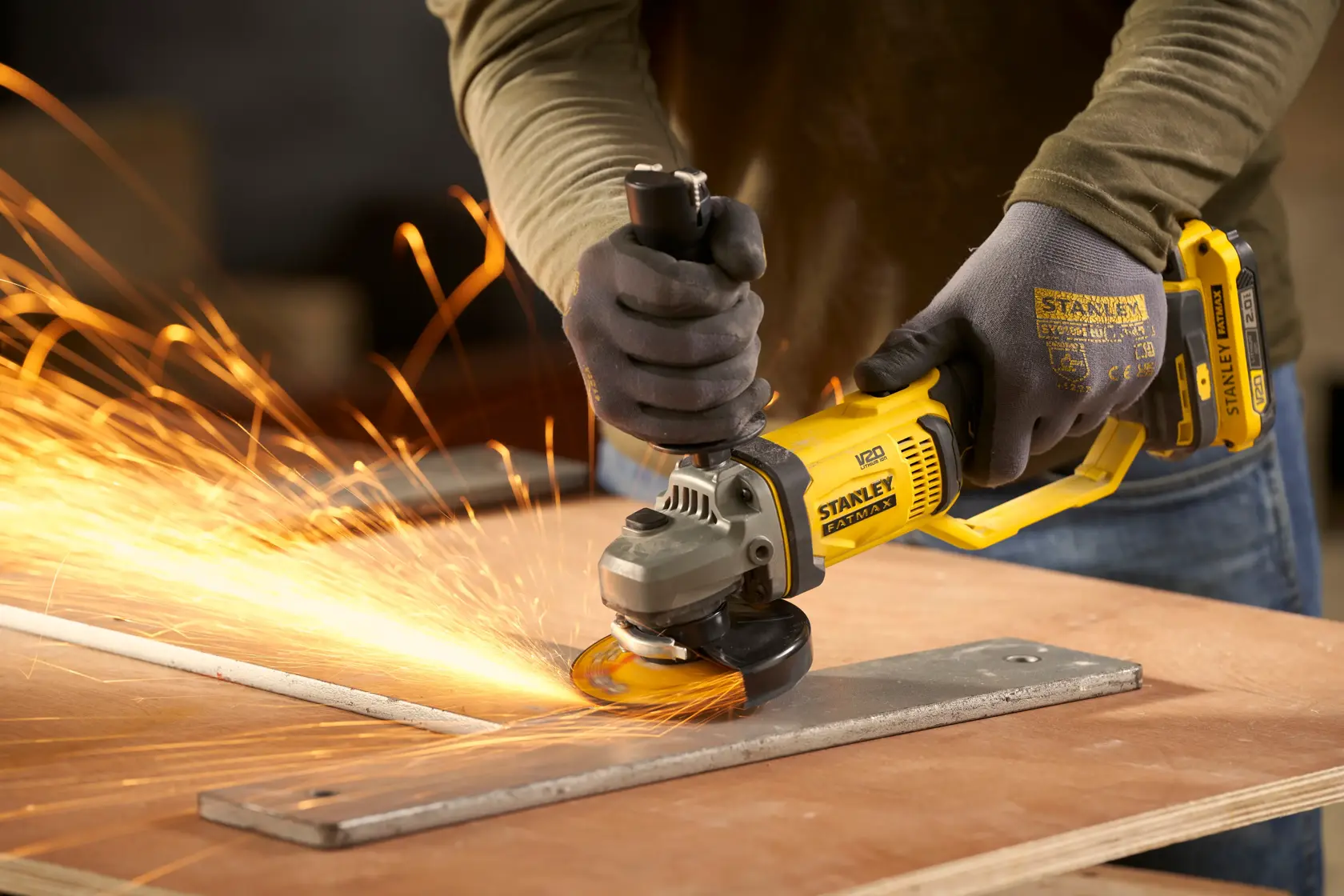 Photo of STANLEY SFMCG300B angle grinder in use, grinding metal with sparks, worker wearing gloves.