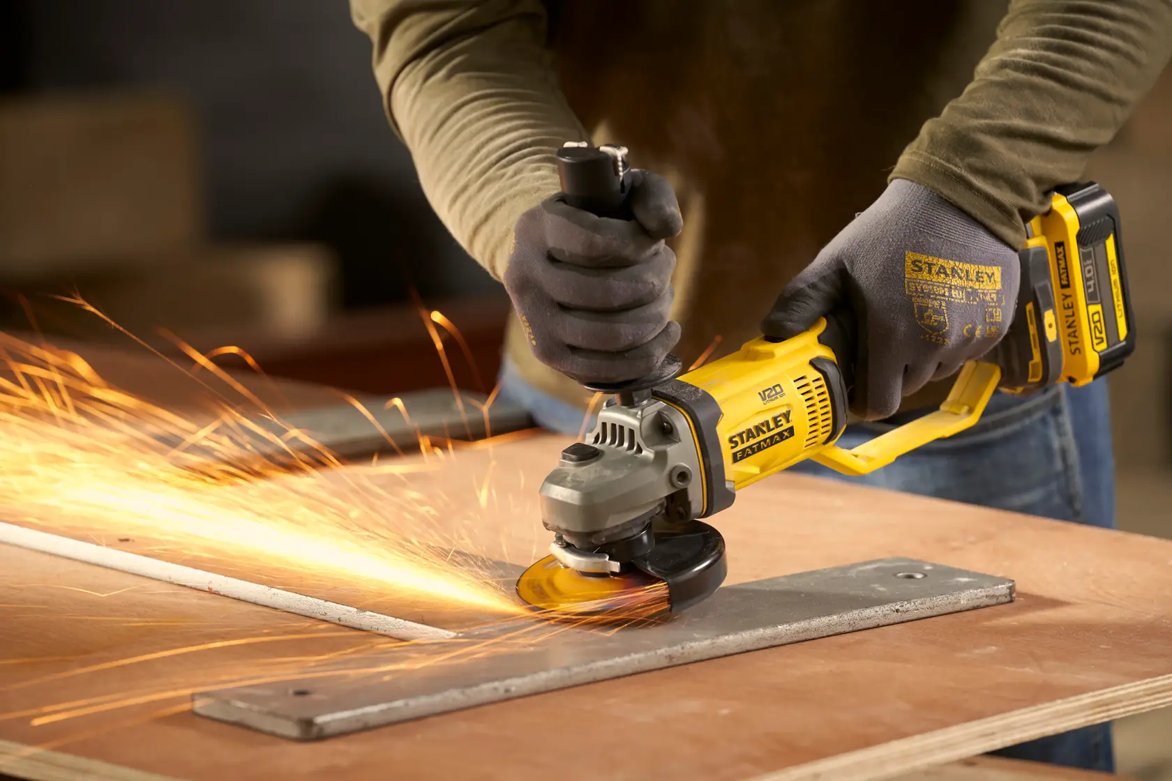 STANLEY SFMCG300B cordless angle grinder in use, grinding metal with sparks, close-up action shot.