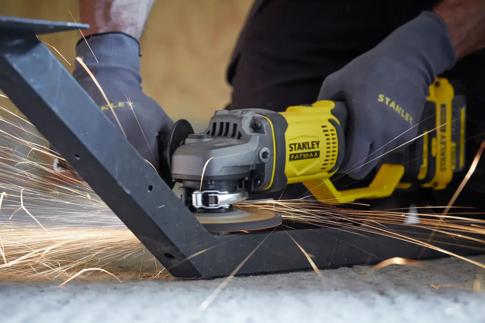 STANLEY SFMCG400B angle grinder in use cutting metal, yellow and black tool with visible sparks.