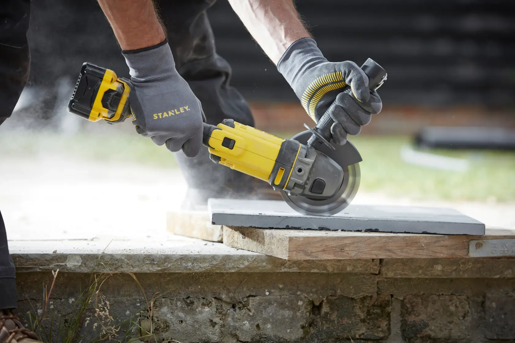 STANLEY SFMCG400B cordless angle grinder in use cutting a concrete slab outdoors.