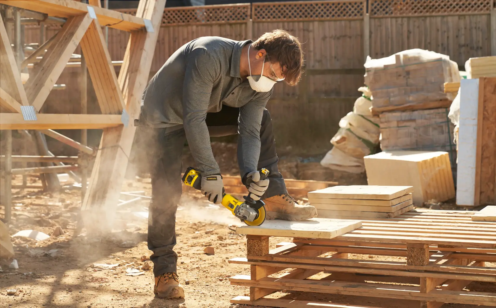 Photo of worker using STANLEY SFMCG710B-XJ angle grinder on construction site, cutting stone slab on pallet.