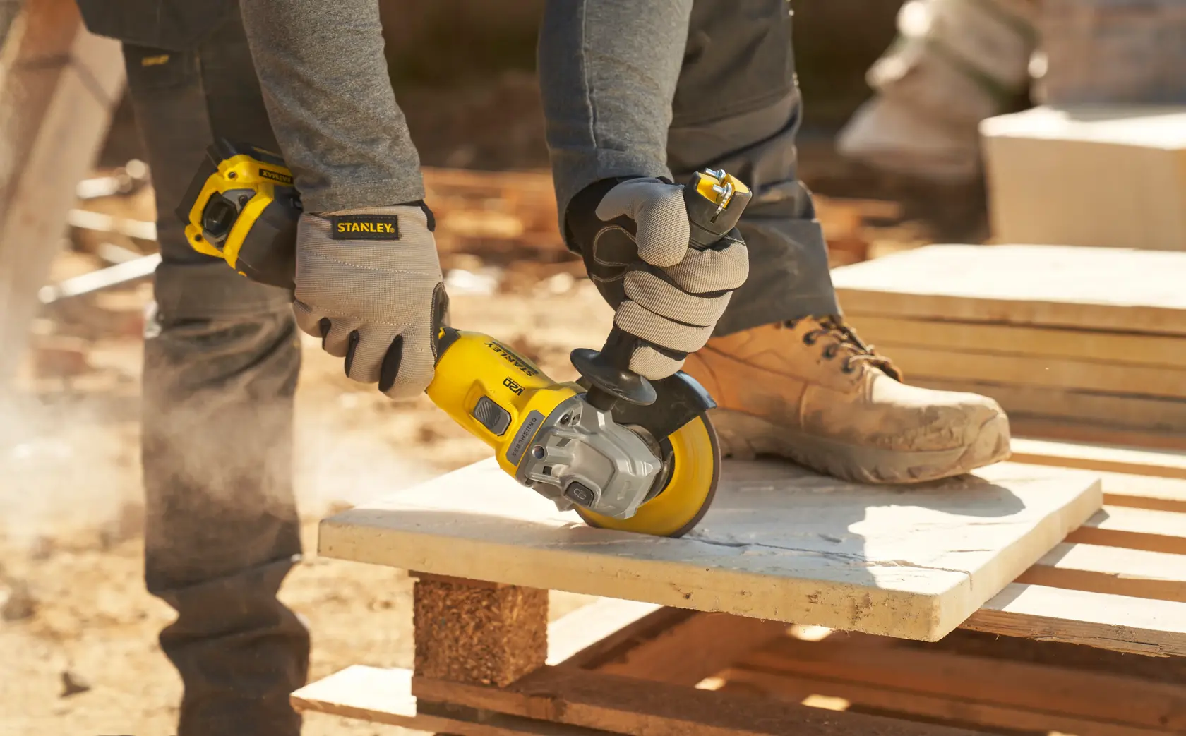 STANLEY SFMCG710B-XJ angle grinder in use, grinding stone slab outdoors, close-up view with gloves.