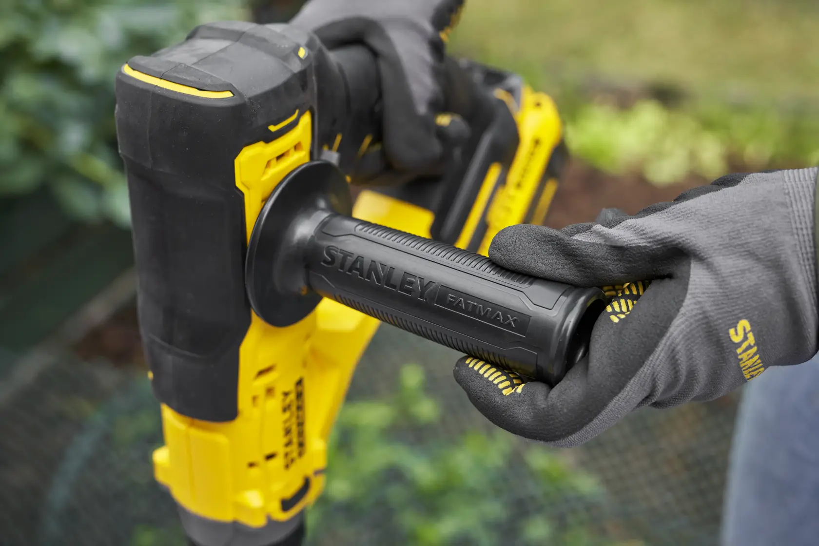 STANLEY SFMCGA75B rotary hammer close-up, black and yellow handle with STANLEY FATMAX branding held by gloved hands.