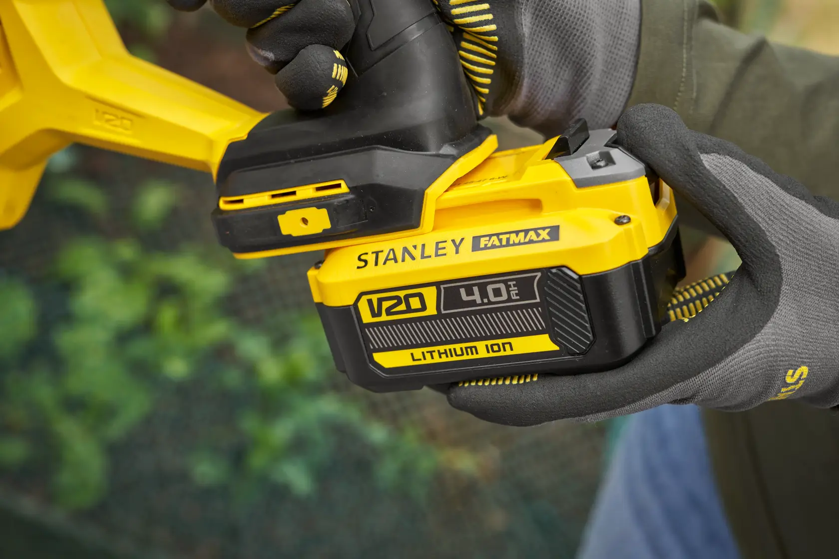 Photo of STANLEY FATMAX SFMCGA75B V20 4.0Ah lithium-ion battery attached to tool, held with gloved hands.