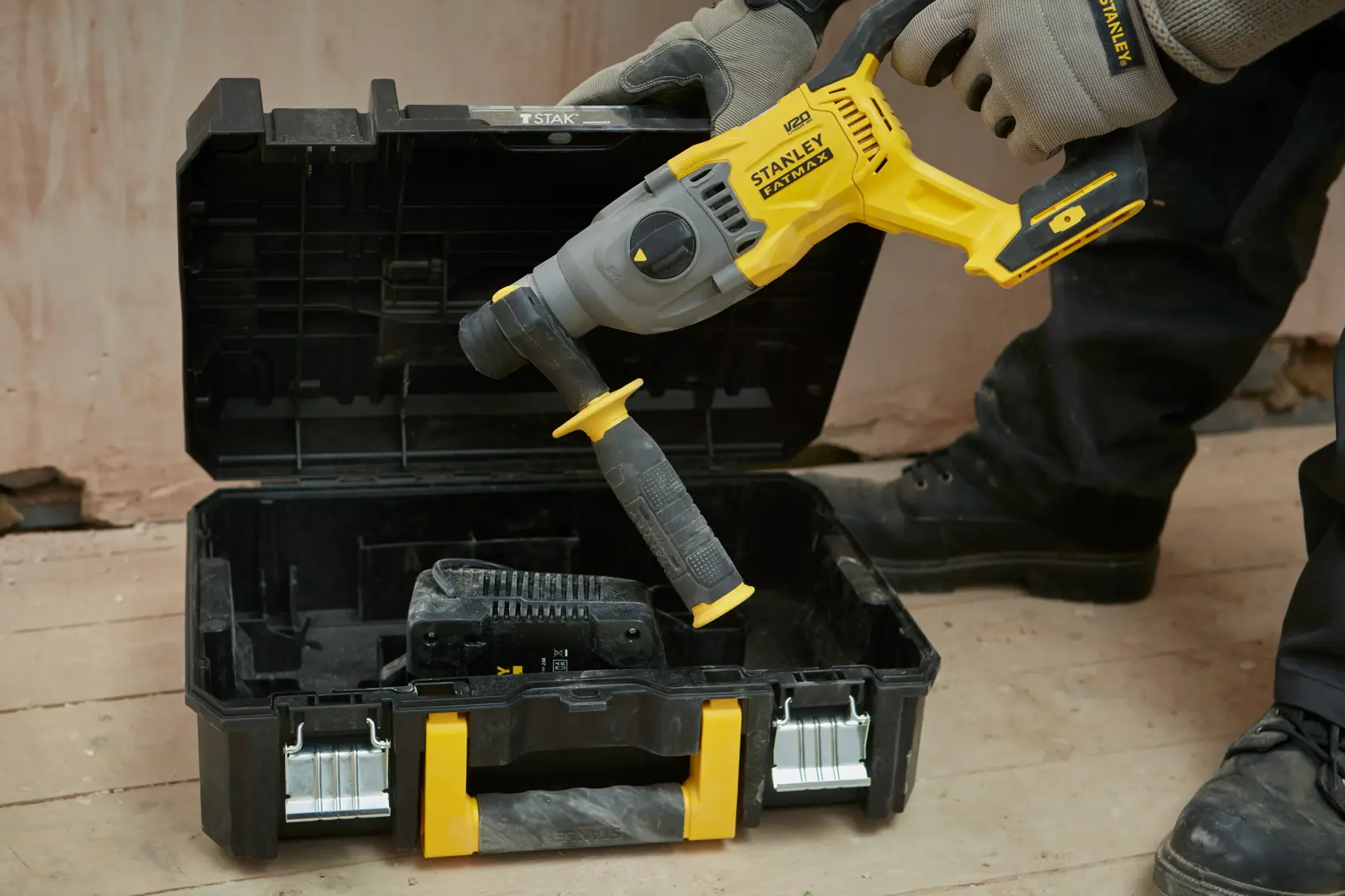 STANLEY SFMCH900B rotary hammer being placed in a black and yellow carrying case on a workshop floor.