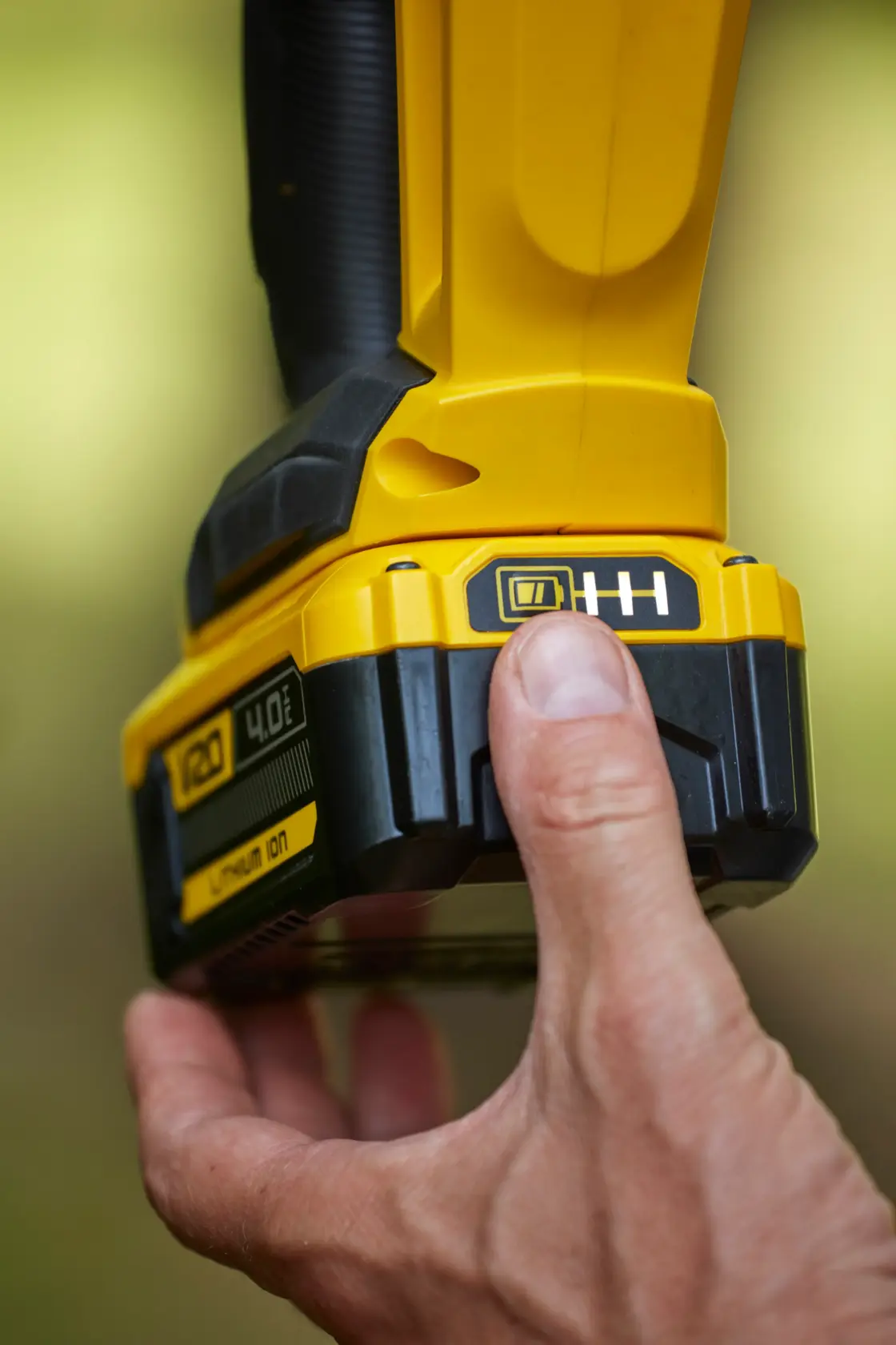 Close-up photo of hand pressing button on STANLEY SFMCHT855M1 cordless tool battery showing power indicator.