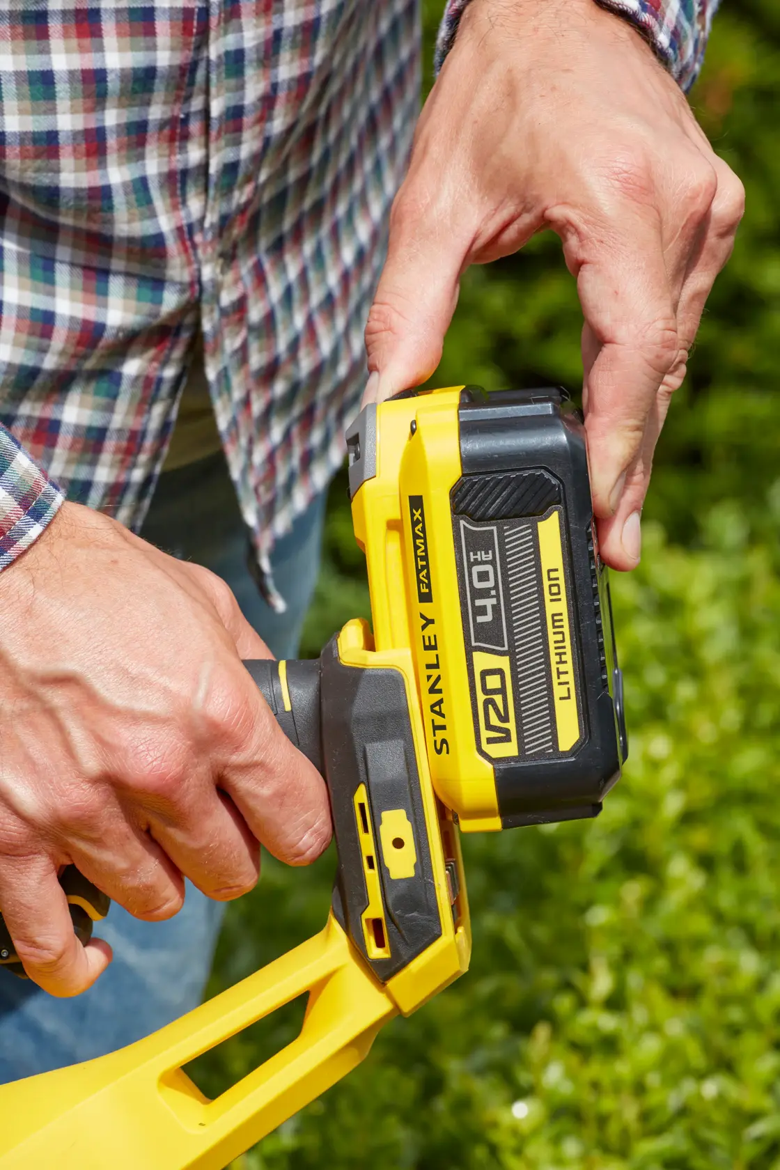 Photo of STANLEY SFMCHT855M1 V20 4.0Ah Lithium-Ion battery being inserted into yellow tool outdoors.