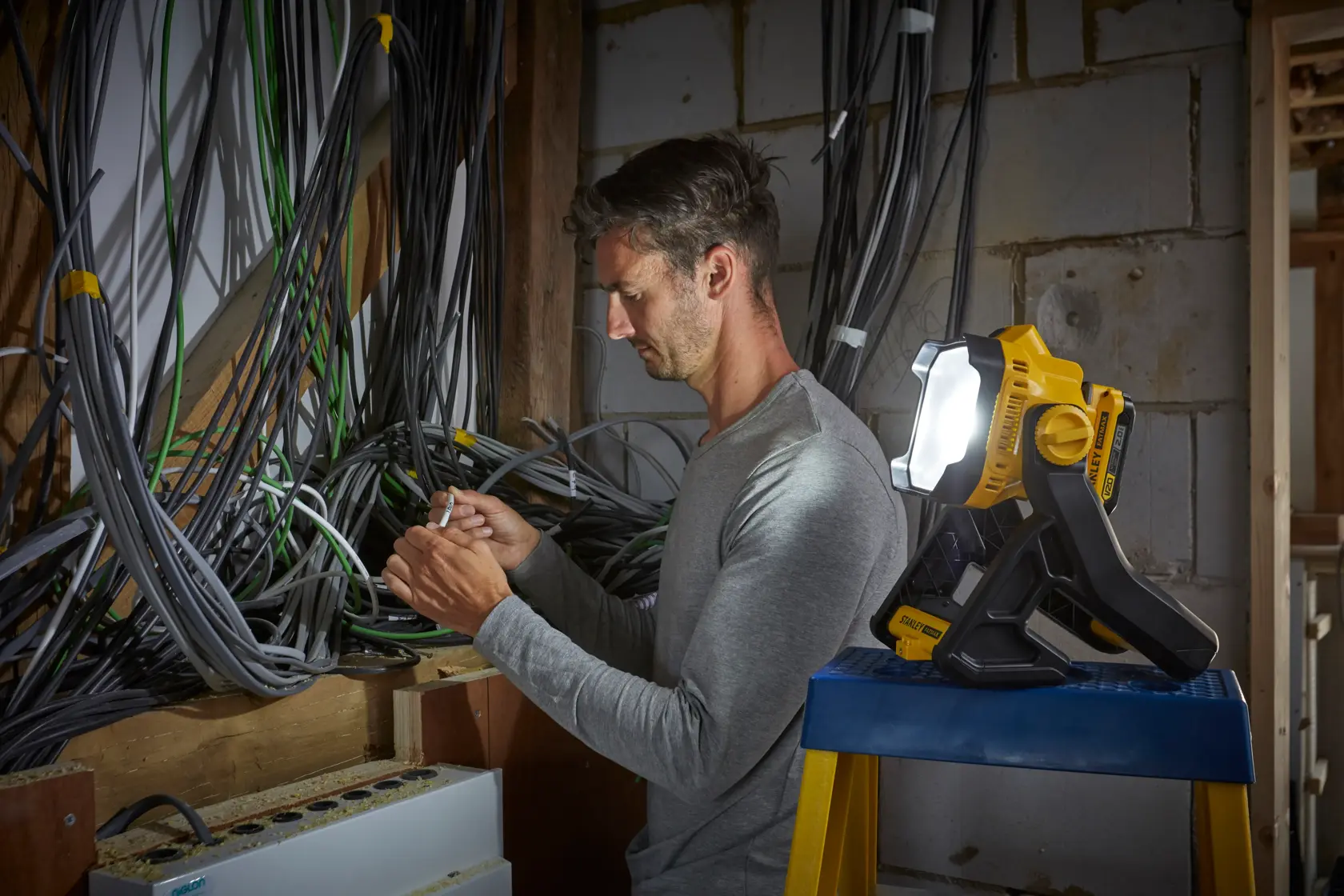Stanley SFMCL030B work light illuminating electrician working amid cables in unfinished wall.
