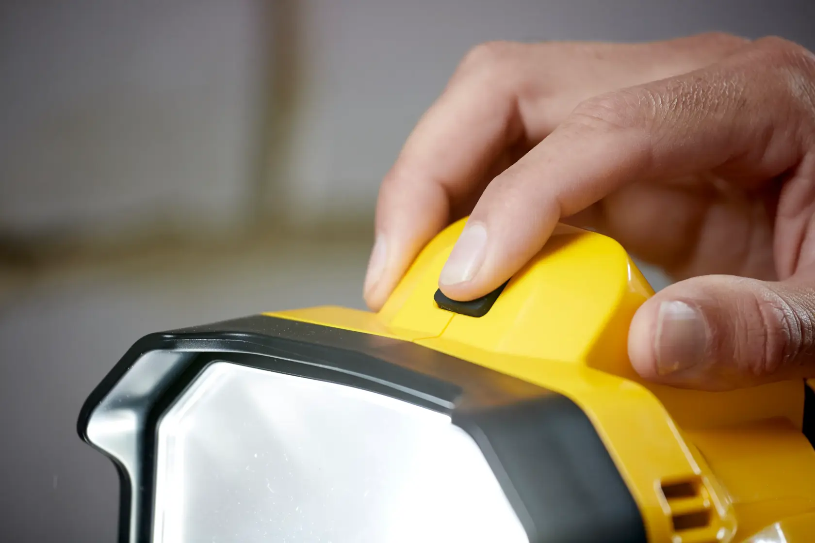 STANLEY SFMCL030B LED work light close-up, finger pressing power button, yellow and black housing.