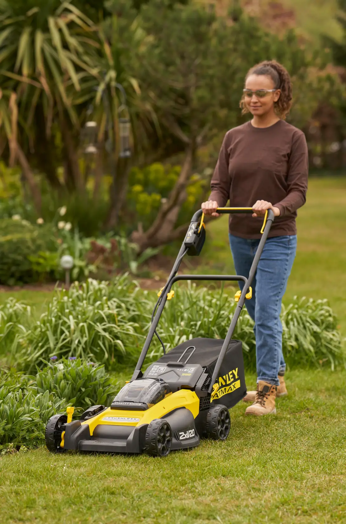 Photo of STANLEY SFMCMW2651M lawn mower in use on grass, yellow and black design, outdoor garden setting.